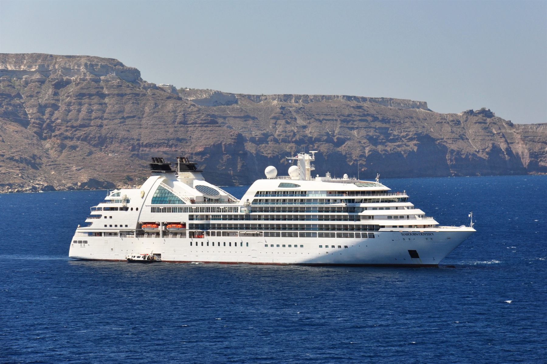 A small luxury cruise ship sailing below the cliffs of a Greek island