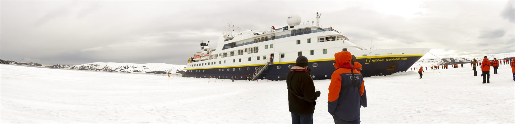 An expedition ship moored at the ice edge, with parka-clad passengers on the snow