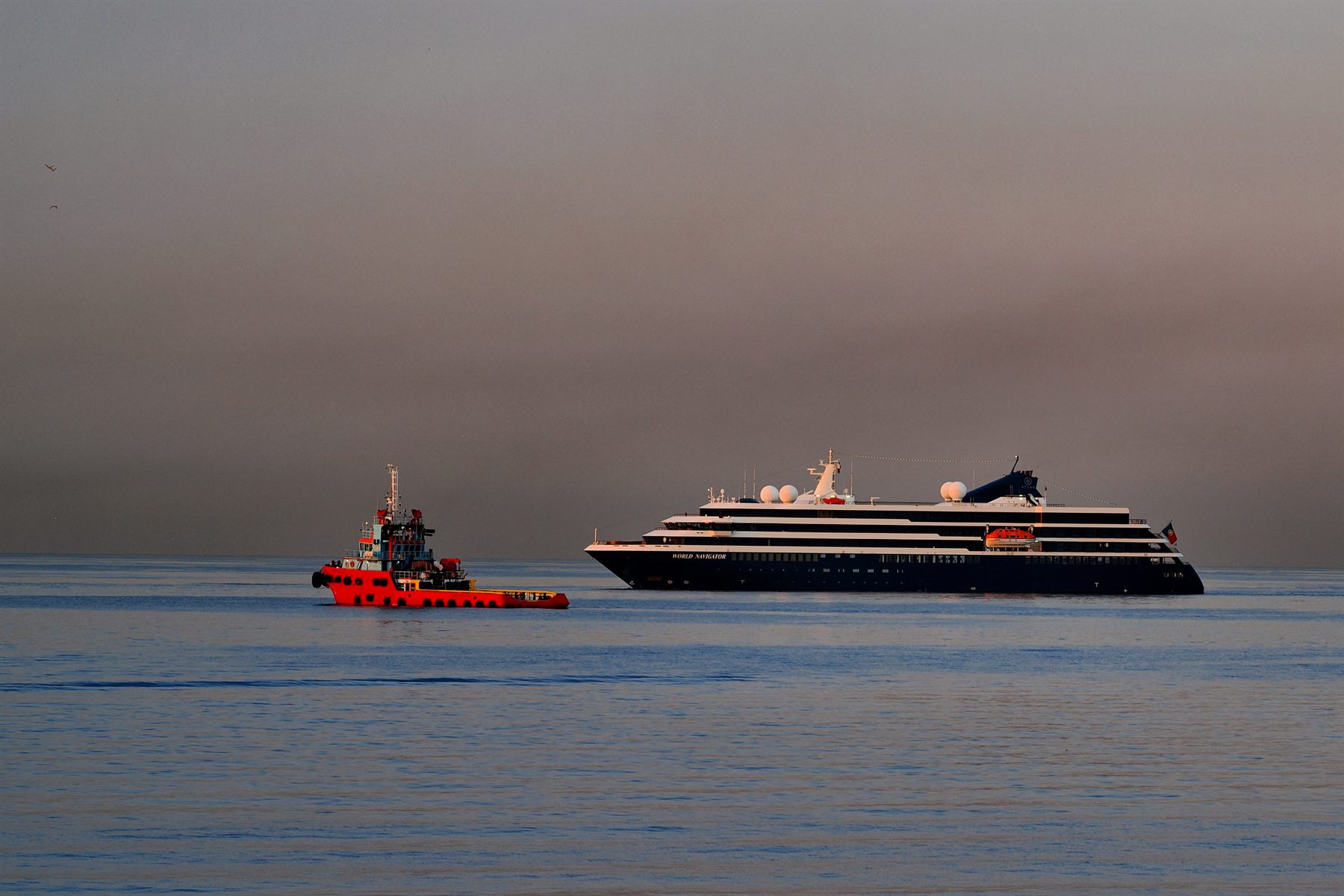 A small Atlas expedition ship and a red tug on calm water